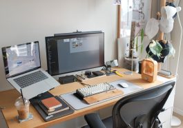 A modern workspace with a laptop and a monitor displaying software, various stationery items, and a plant.
