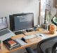 A modern workspace with a laptop and a monitor displaying software, various stationery items, and a plant.