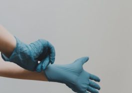 A hand putting on a blue medical glove against a plain background.