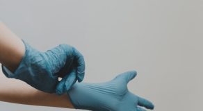 A hand putting on a blue medical glove against a plain background.