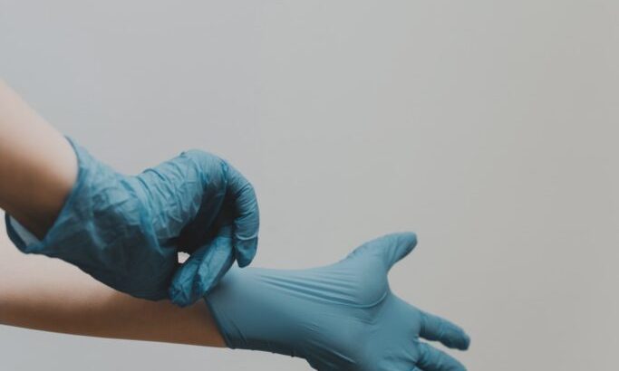 A hand putting on a blue medical glove against a plain background.