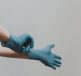 A hand putting on a blue medical glove against a plain background.